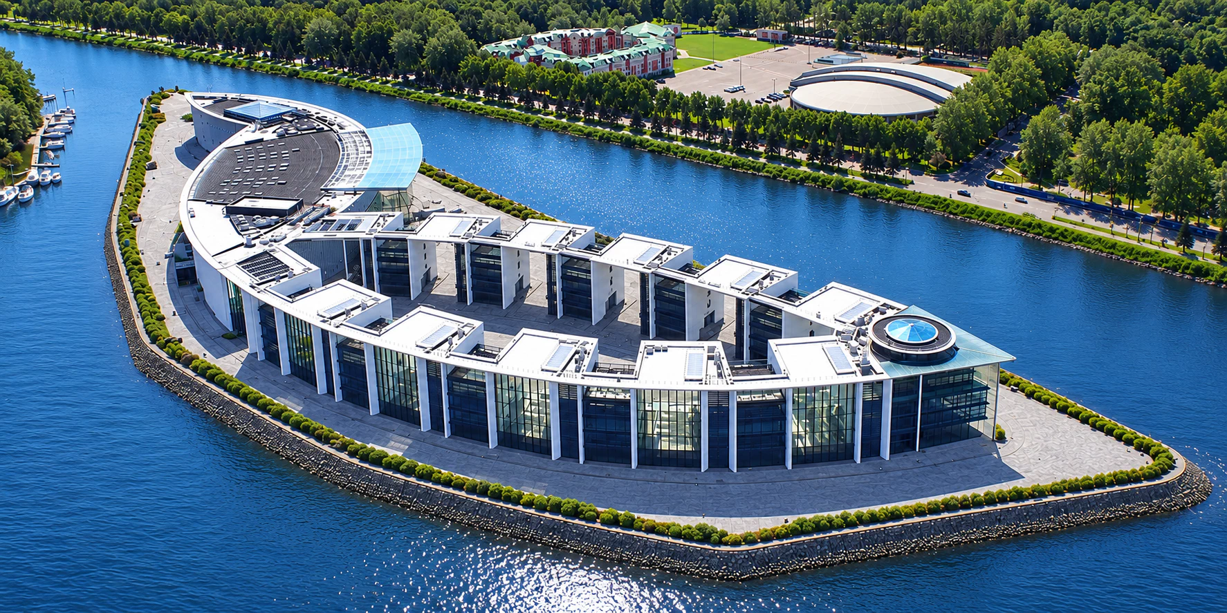 Aerial panoramic view of a curved waterfront building with repeated glazed bays, projecting roof and surrounding waterways